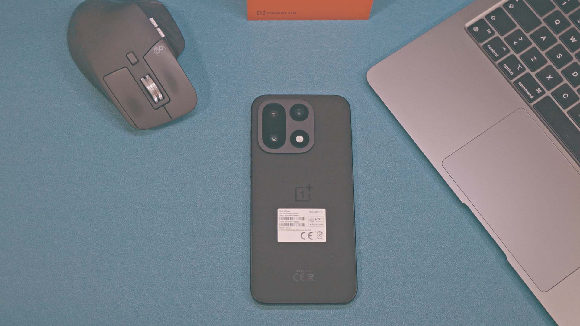 Zadnja strana OnePlus 15 uređaja na plavoj pozadini prikazujući kameru i novi dizajn